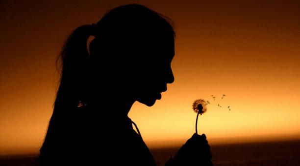A silhouette of a person blowing a dandelion
Description automatically generated