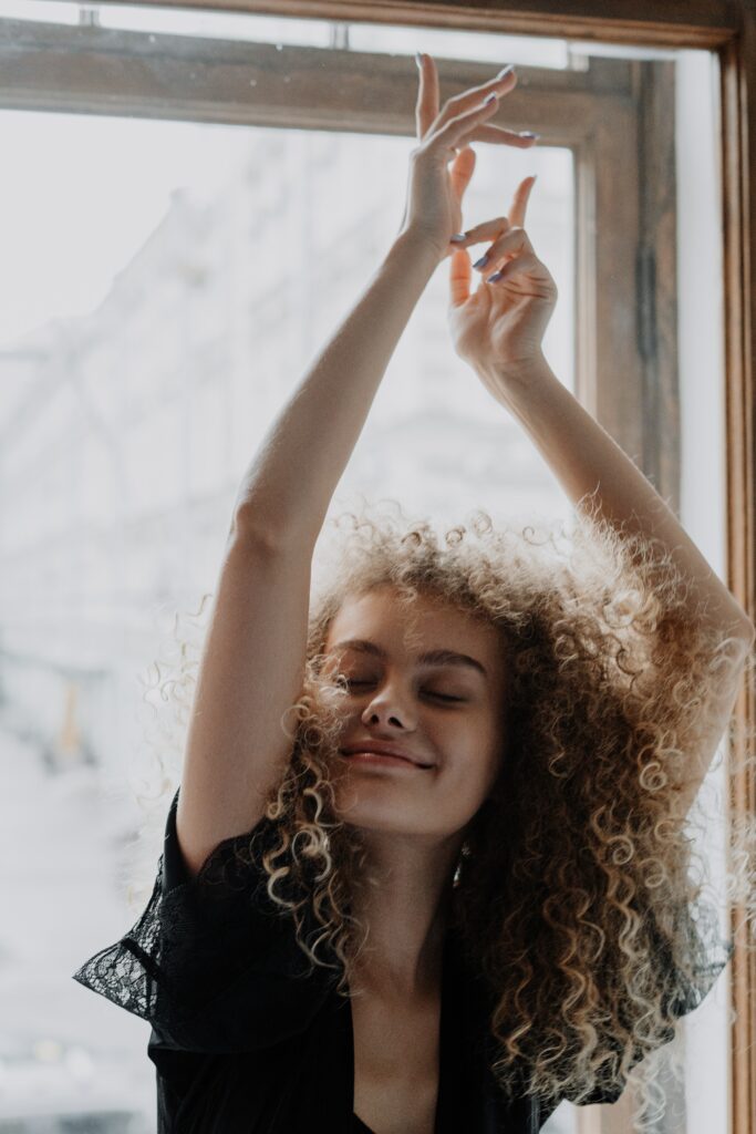 A person with curly hair holding up her hands
Description automatically generated