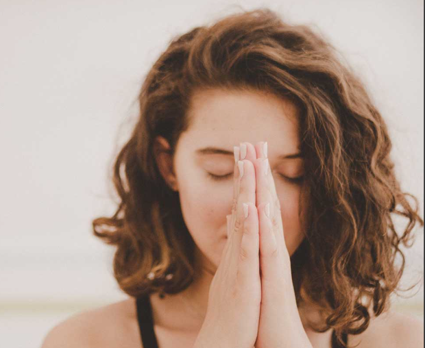 A person with her hands together in front of her face

Description automatically generated